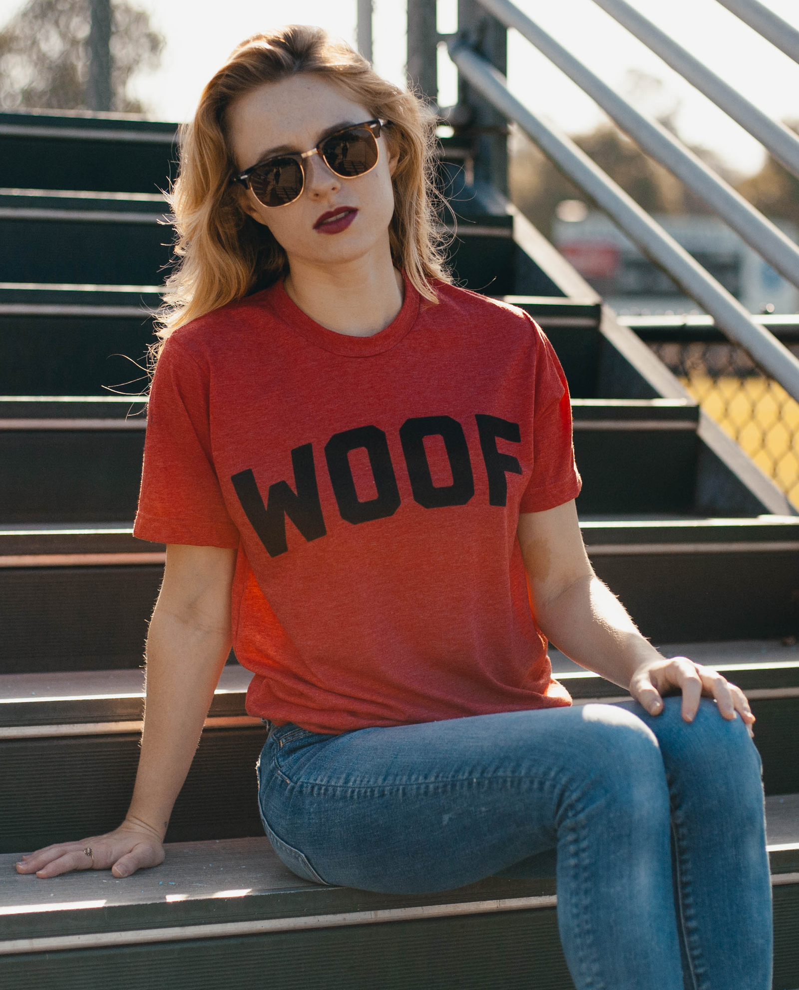 Woman in sunglasses sitting on steps and wearing red WOOF shirt