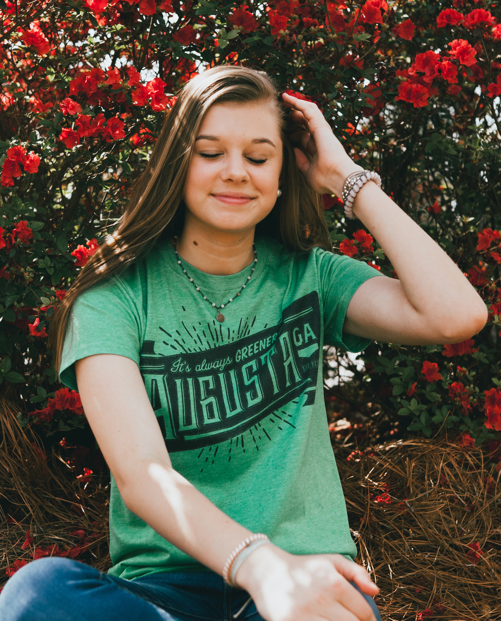 Girl sitting in front of flowers with eyes closed and wearing Always Greener shirt