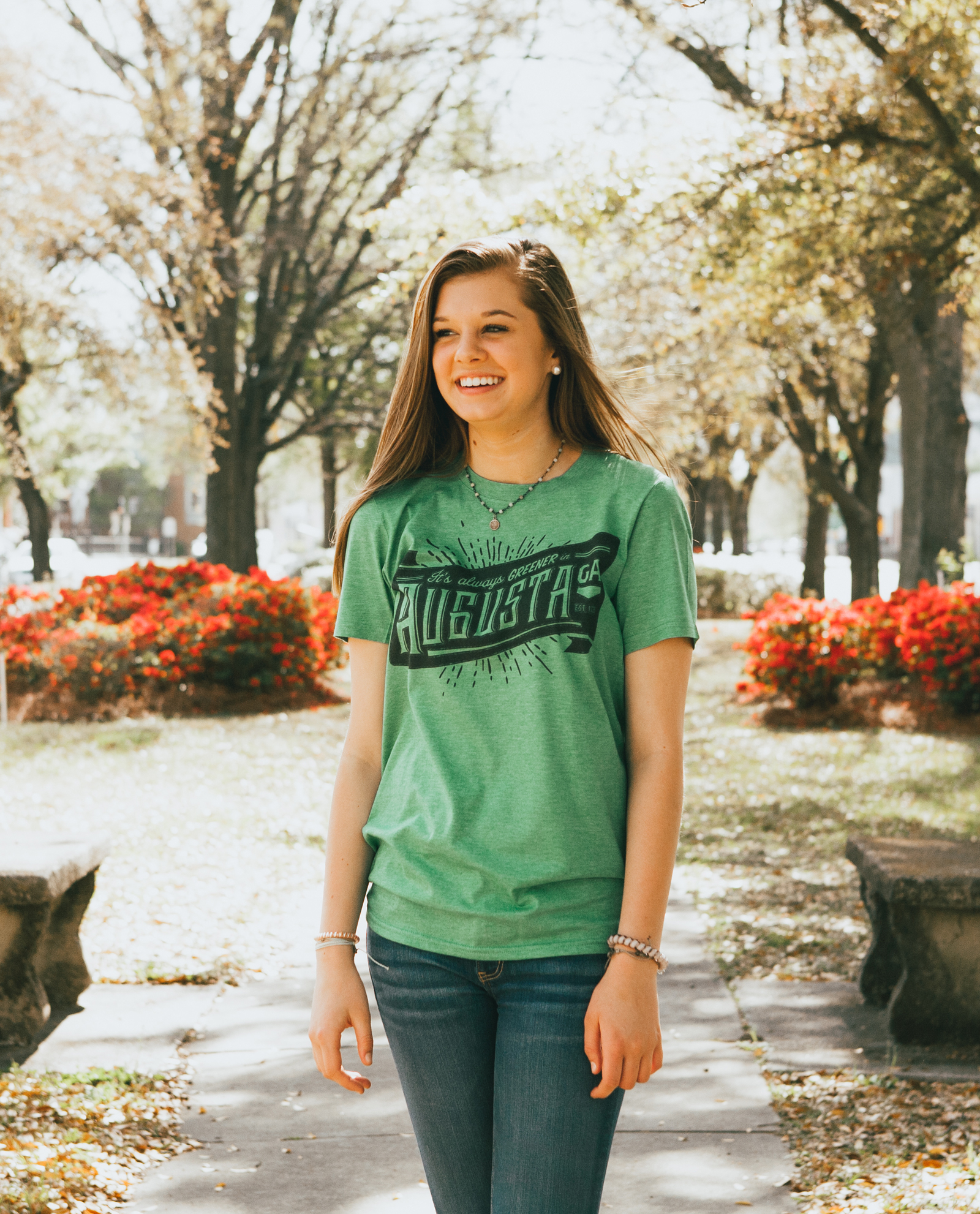 Girl wearing green Always Greener shirt on sidewalk in front of flowers