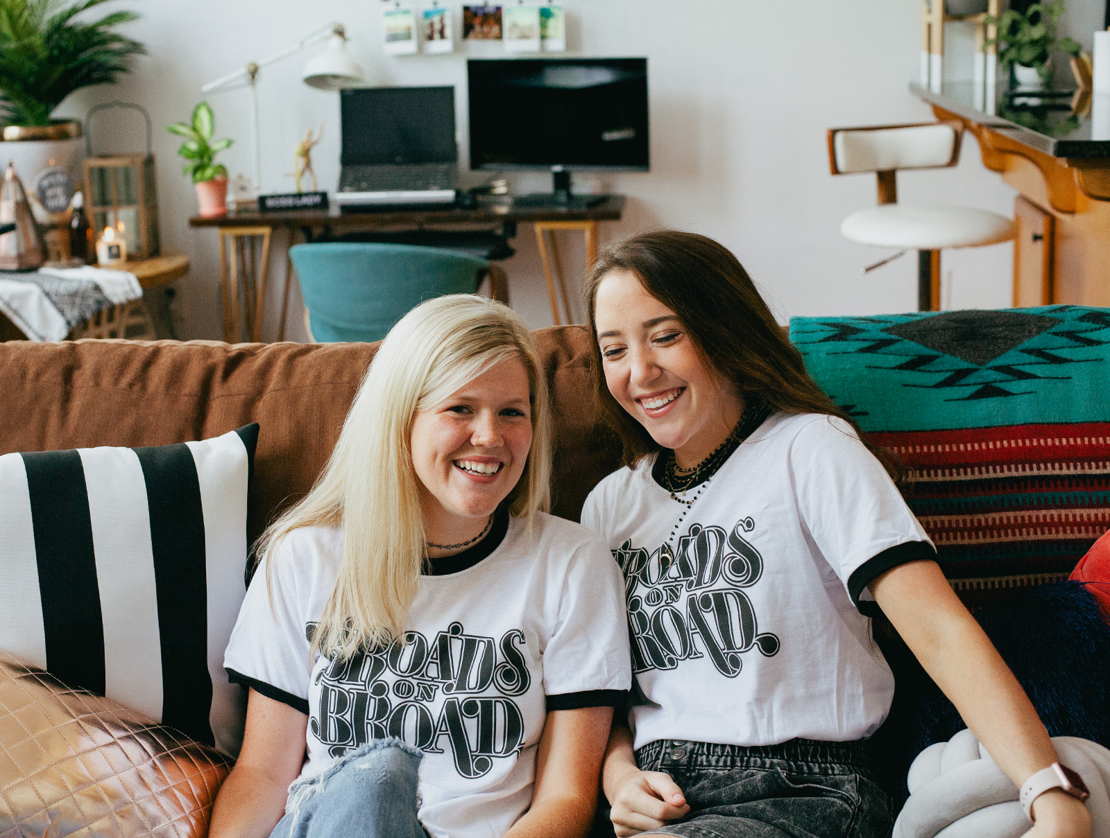 Two women sitting on a couch and wearing Broads on Broad shirts