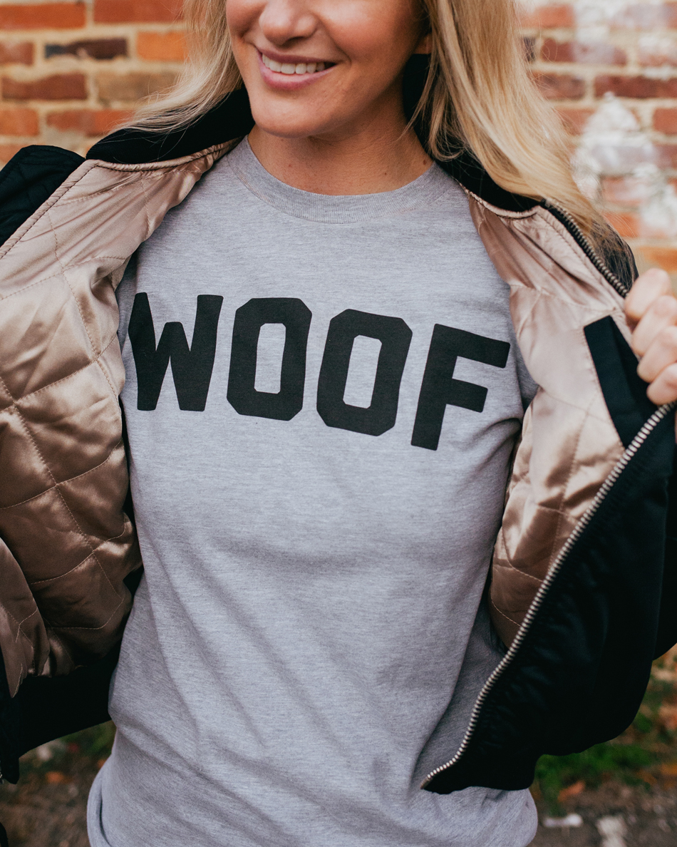 Woman wearing gray long sleeve WOOF shirt with black jacket
