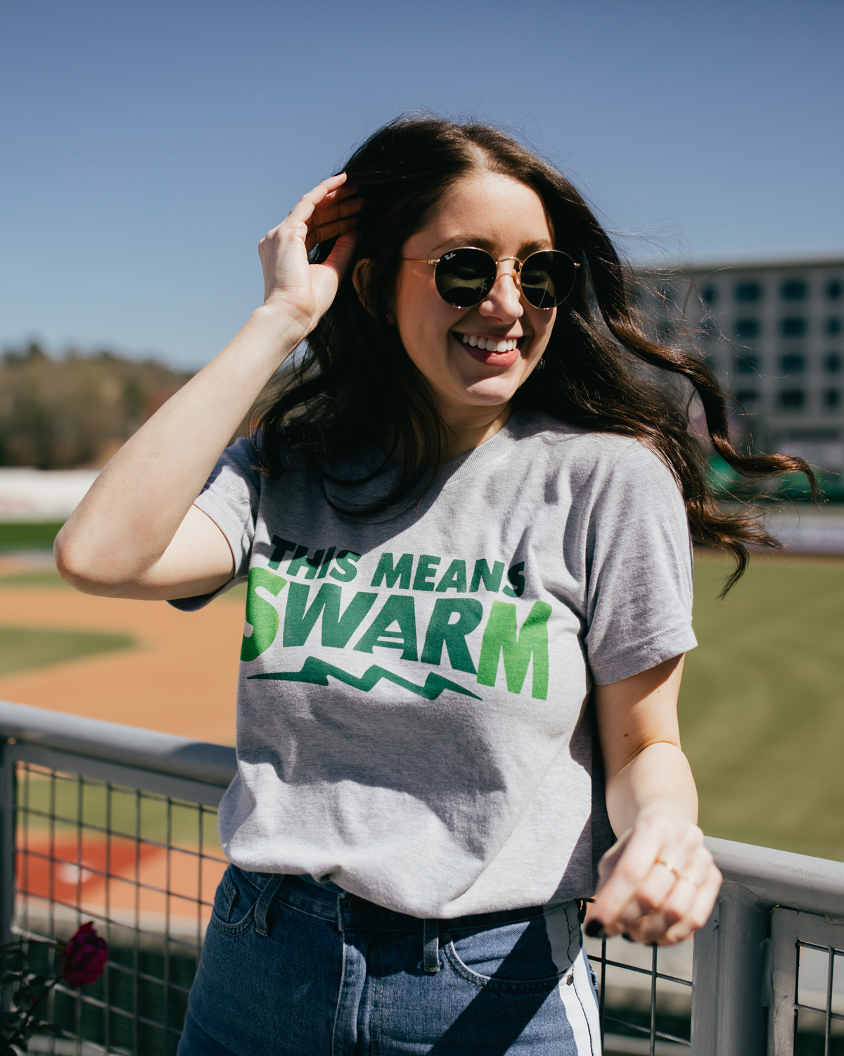 Woman wearing gray Augusta Green Jackets Swarm shirt and smiling at the ballpark
